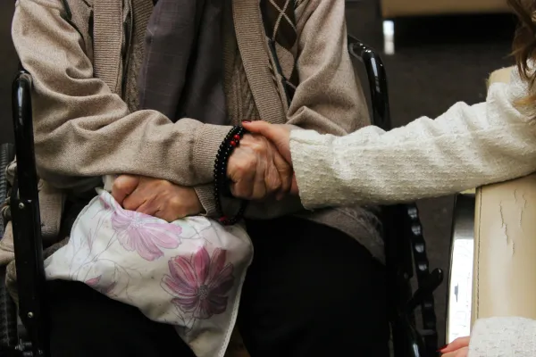 One person sits in a wheelchair while another holds their hand supportively